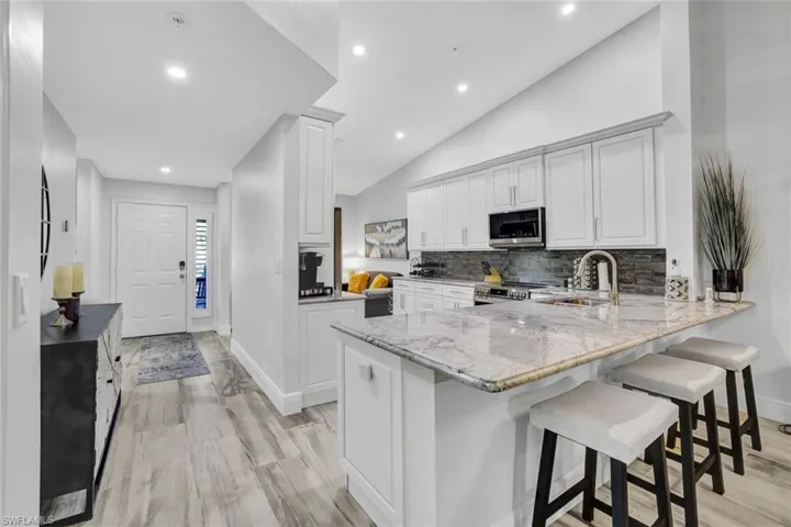 Kitchen with kitchen peninsula, a kitchen breakfast bar, light stone countertops, vaulted ceiling, and stainless steel appliances