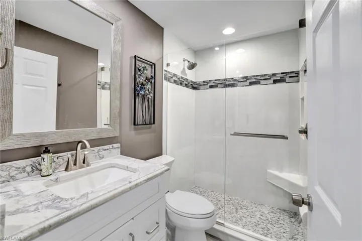 Bathroom featuring a shower with door, vanity, and toilet