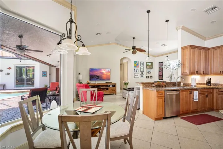 Kitchen featuring vaulted ceiling, hanging light fixtures, a ceiling fan, dark stone counters, and crown molding