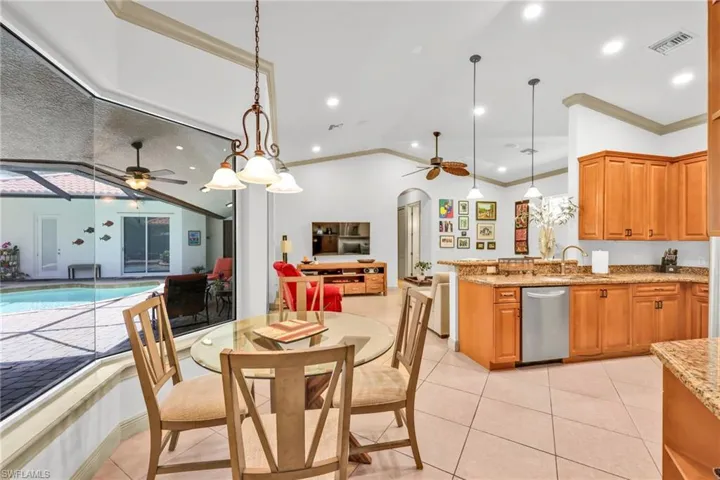 Kitchen featuring stainless steel dishwasher, open floor plan, ceiling fan, ornamental molding, and light stone counters