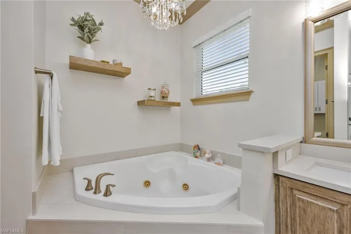 Full bath featuring vanity, a jetted tub, and a chandelier