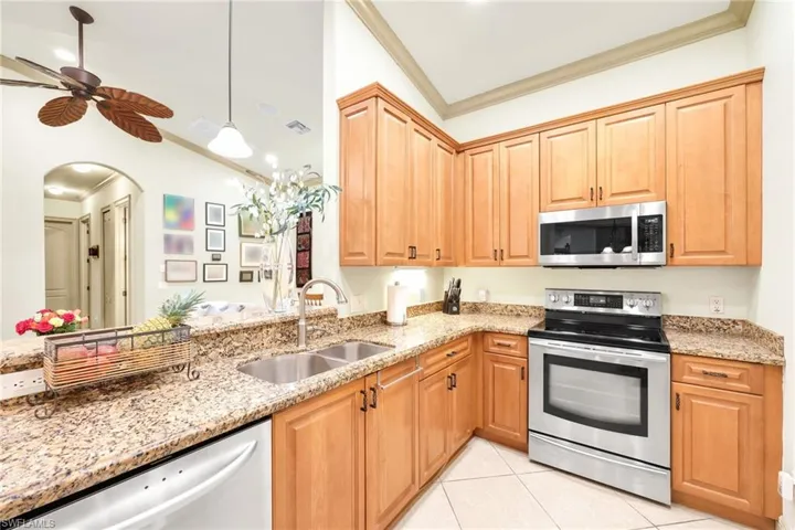 Kitchen with appliances with stainless steel finishes, crown molding, light stone countertops, light tile patterned floors, and pendant lighting