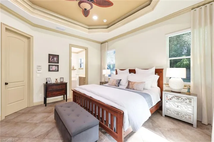 Bedroom featuring a raised ceiling, crown molding, ceiling fan, ensuite bath, and light tile patterned flooring