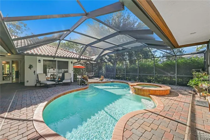 View of swimming pool featuring a patio area, glass enclosure, a pool with connected hot tub, and a sunroom