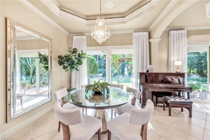 Tiled dining space featuring crown molding, a raised ceiling, plenty of natural light, and a chandelier