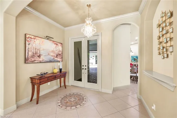 Entrance foyer featuring arched walkways, light tile patterned floors, crown molding, and a chandelier