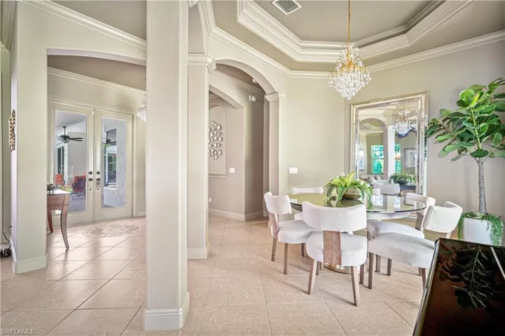 Dining room featuring arched walkways, crown molding, light tile patterned floors, a chandelier, and french doors