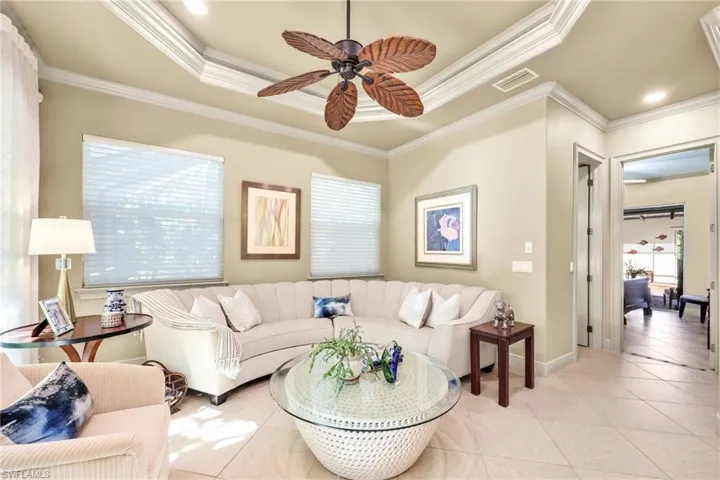 Living area featuring a raised ceiling, tile patterned floors, a ceiling fan, and ornamental molding