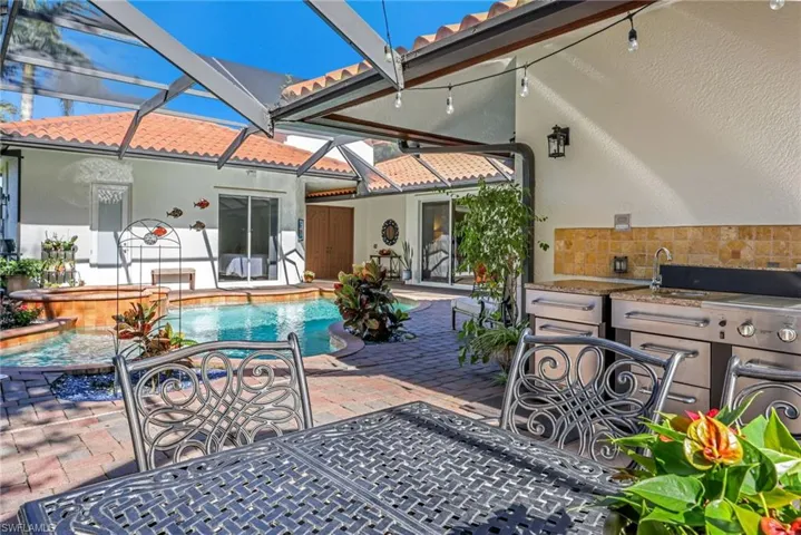 Rear view of property featuring a tiled roof, stucco siding, a patio area, exterior kitchen, and an outdoor pool