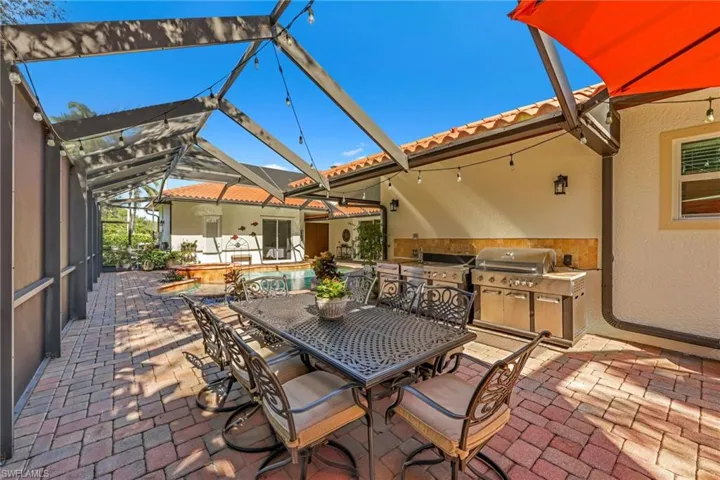 View of patio / terrace featuring a lanai, outdoor dining area, a sunroom, an outdoor kitchen, and a pool with connected hot tub