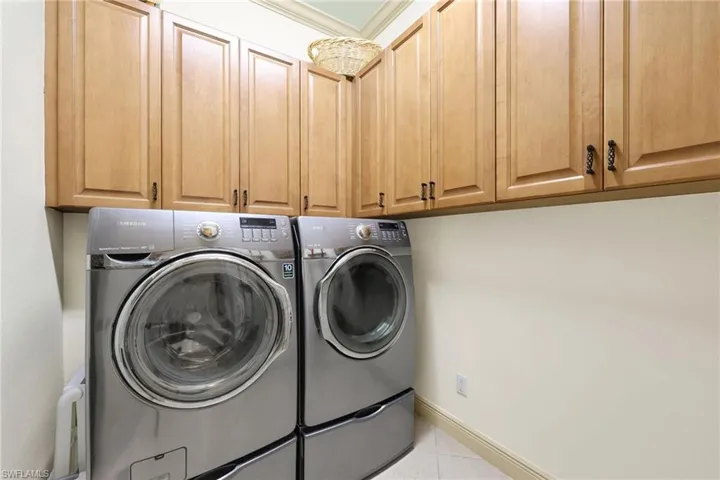 Laundry area featuring light tile patterned floors, separate washer and dryer, and cabinet space