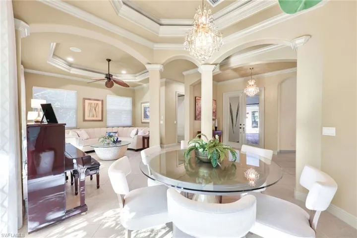 Tiled dining space with a raised ceiling, arched walkways, a chandelier, crown molding, and ceiling fan