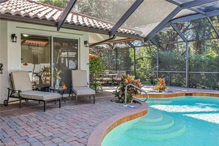 Swimming pool with glass enclosure, a patio area, a sunroom, and view of scattered trees