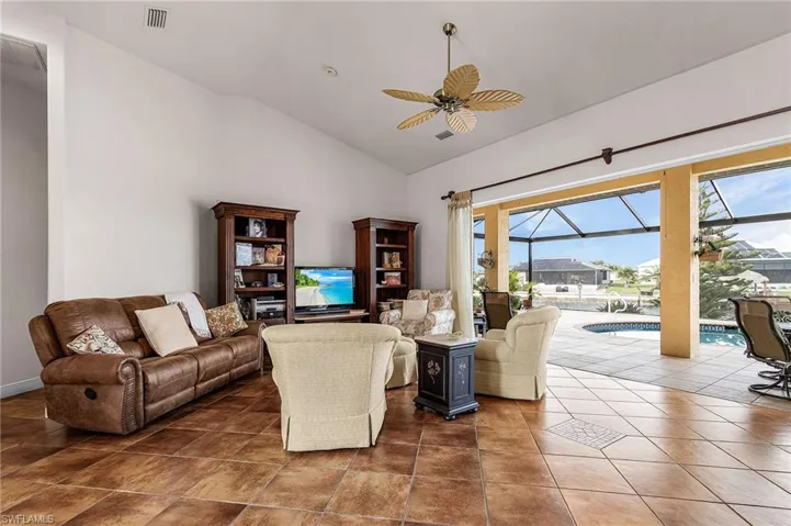 Living room with a sunroom, a ceiling fan, dark tile patterned flooring, and high vaulted ceiling