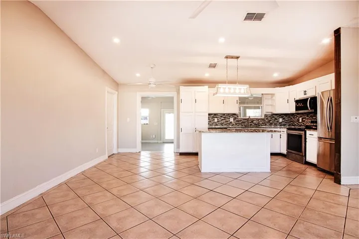 Kitchen featuring white cabinetry, pendant lighting, appliances with stainless steel finishes, light tile patterned floors, and a kitchen island