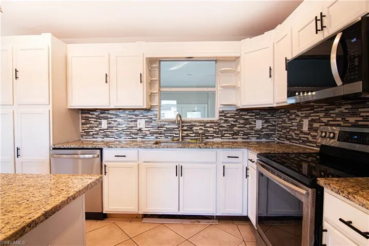 Kitchen with appliances with stainless steel finishes, open shelves, white cabinetry, and light stone counters