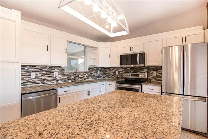 Kitchen featuring stainless steel appliances, white cabinetry, light stone countertops, open shelves, and tasteful backsplash