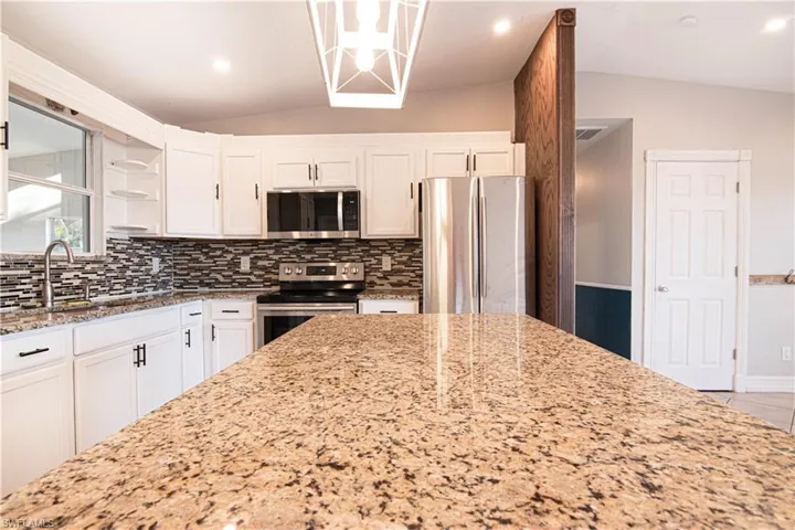 Kitchen with vaulted ceiling, white cabinets, stainless steel appliances, light stone counters, and recessed lighting