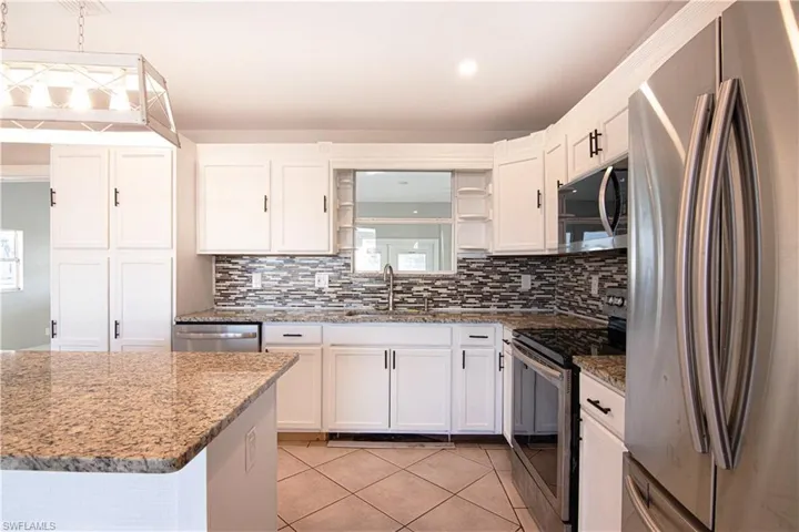 Kitchen with appliances with stainless steel finishes, white cabinetry, light stone countertops, light tile patterned floors, and tasteful backsplash