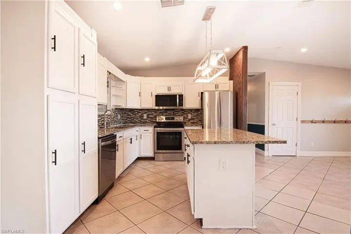 Kitchen featuring vaulted ceiling, backsplash, appliances with stainless steel finishes, decorative light fixtures, and a kitchen bar