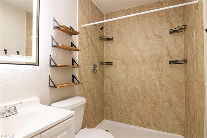 Full bathroom with a textured wall, vanity, and a tile shower