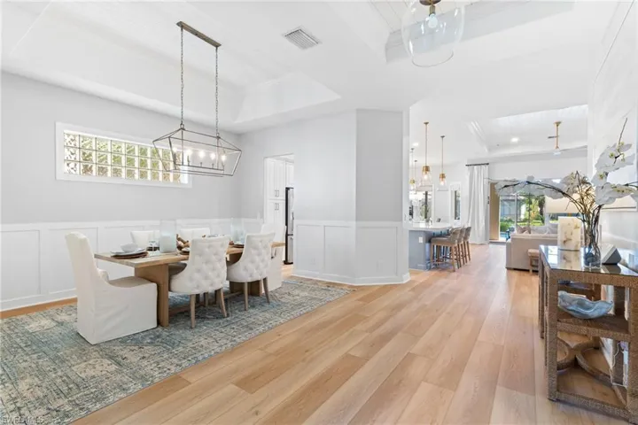 Dining area with crown molding, a tray ceiling, a chandelier, and light wood-style flooring