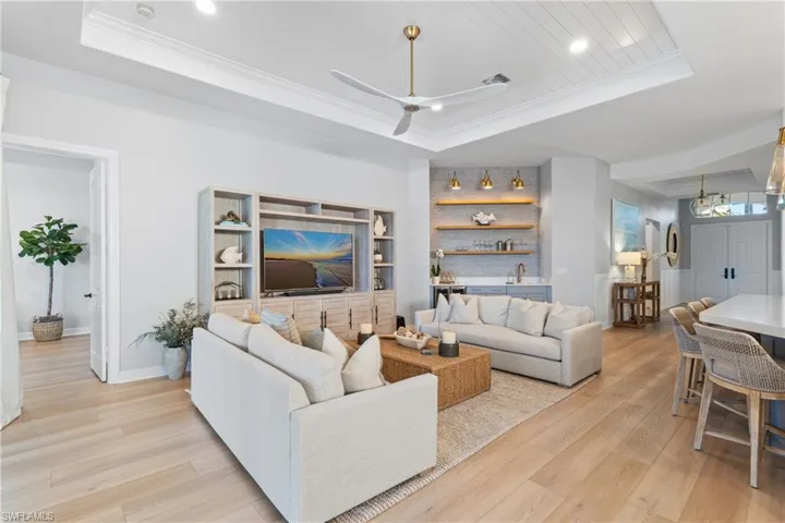 Living room with a raised ceiling, crown molding, ceiling fan, and light hardwood / wood-style flooring