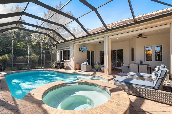 View of pool featuring ceiling fan, glass enclosure, a patio area, area for grilling, and an in ground hot tub