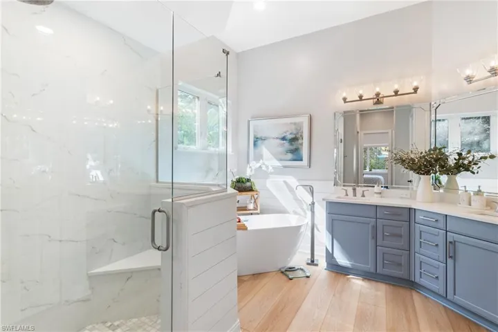 Bathroom featuring vanity, wood-type flooring, independent shower and soaking bath, and a healthy amount of sunlight