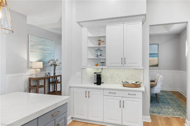 Coffee Bar featuring light white cabinets, light stone counters, decorative backsplash and gold hardware