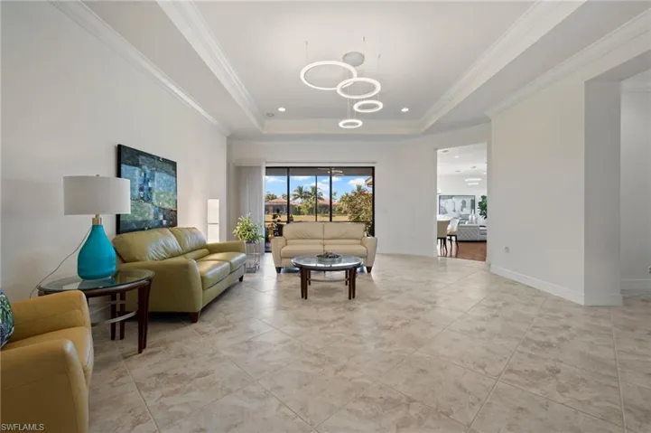 Tiled living room with a notable chandelier, crown molding, and a raised ceiling