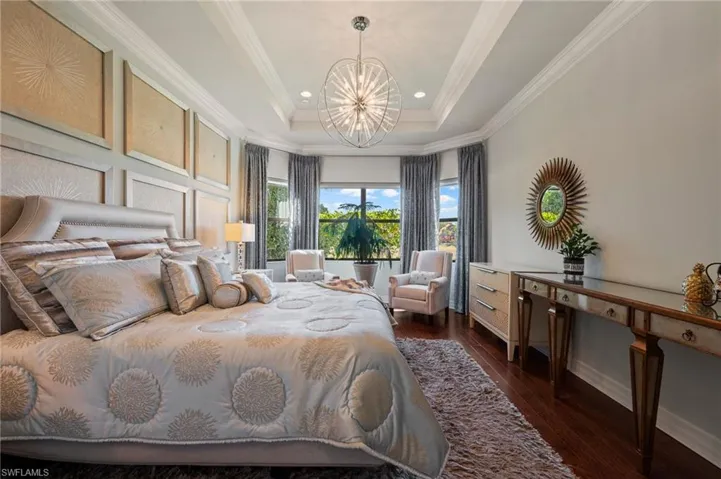 Bedroom with an inviting chandelier, ornamental molding, dark hardwood / wood-style flooring, and a raised ceiling