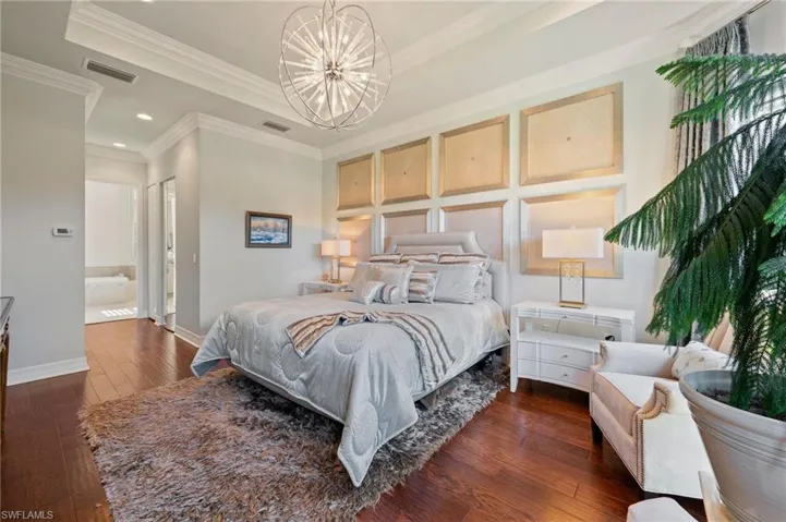 Bedroom with dark hardwood / wood-style floors, a tray ceiling, an inviting chandelier, and crown molding