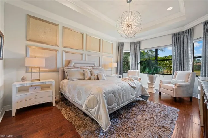 Bedroom with ornamental molding, dark wood-type flooring, a chandelier, and a tray ceiling