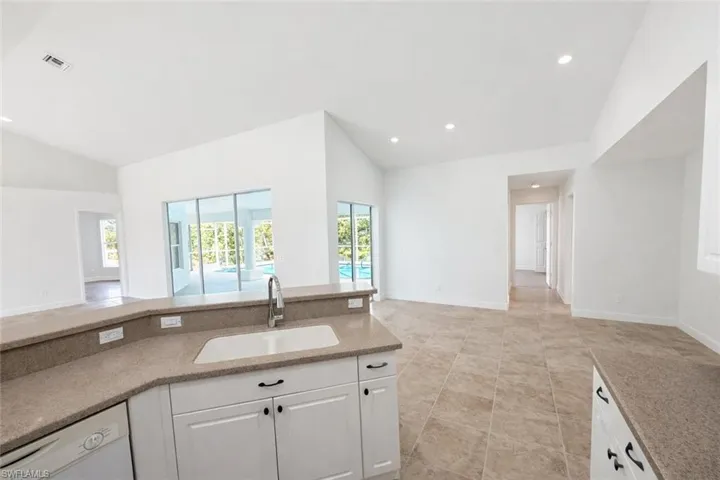 Kitchen with open floor plan, light stone counters, vaulted ceiling, white dishwasher, and white cabinets