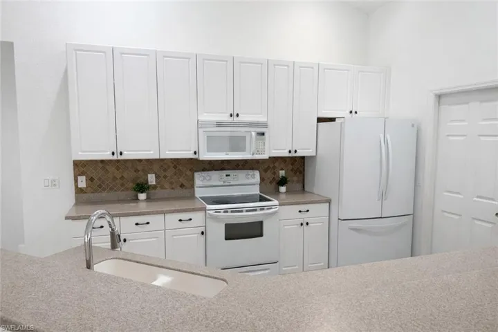 Kitchen featuring white appliances, white cabinets, tasteful backsplash, and light stone counters