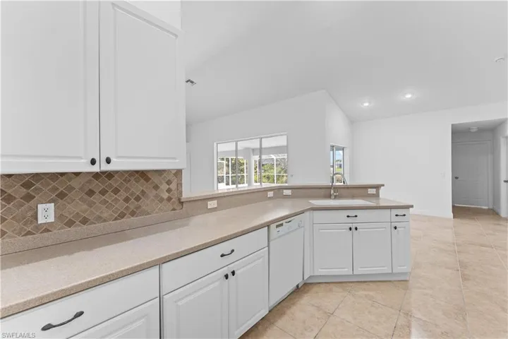 Kitchen with white cabinets, dishwasher, lofted ceiling, a peninsula, and light stone counters