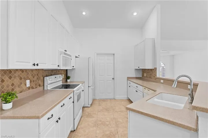 Kitchen with white appliances, white cabinetry, a peninsula, backsplash, and recessed lighting