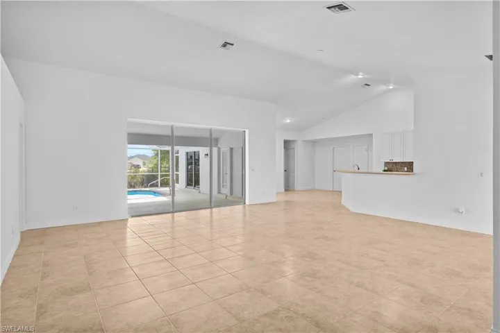 Unfurnished living room with vaulted ceiling, light tile patterned flooring, and a sunroom