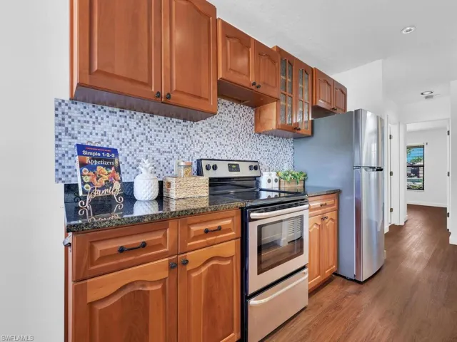 Kitchen with dark hardwood / wood-style floors, tasteful backsplash, dark stone countertops, and stainless steel appliances