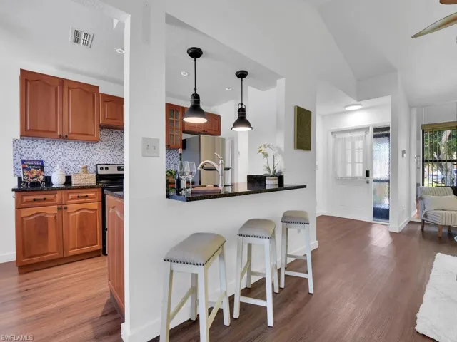Kitchen with stainless steel fridge, wood-type flooring, pendant lighting, tasteful backsplash, and vaulted ceiling