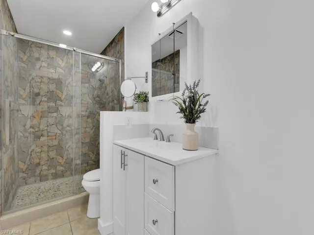 Bathroom featuring a shower with door, tile flooring, toilet, and vanity