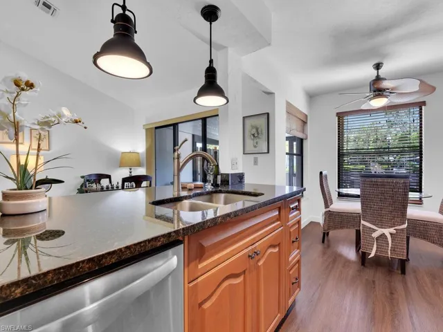 Kitchen with hardwood / wood-style floors, dishwasher, dark stone countertops, hanging light fixtures, and sink