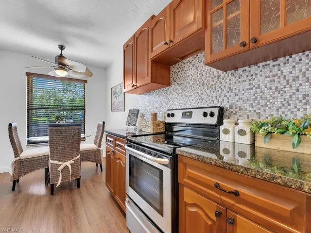 Kitchen with ceiling fan, light hardwood / wood-style flooring, dark stone countertops, backsplash, and stainless steel range with electric stovetop