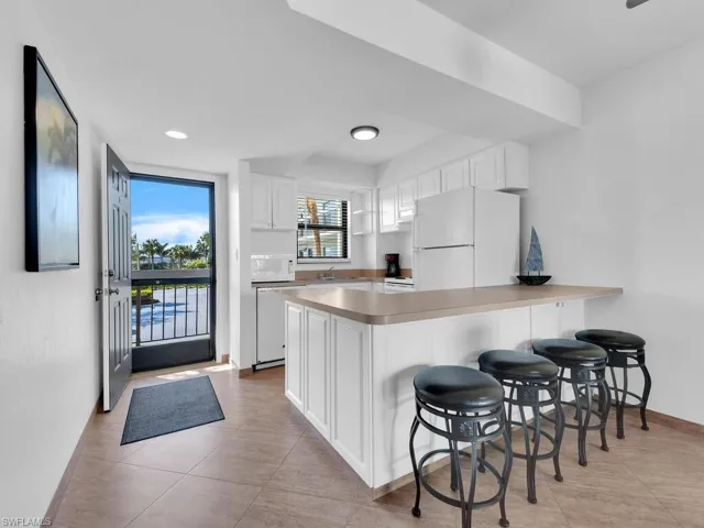 Kitchen featuring a breakfast bar, white appliances, kitchen peninsula, light tile patterned floors, and white cabinetry