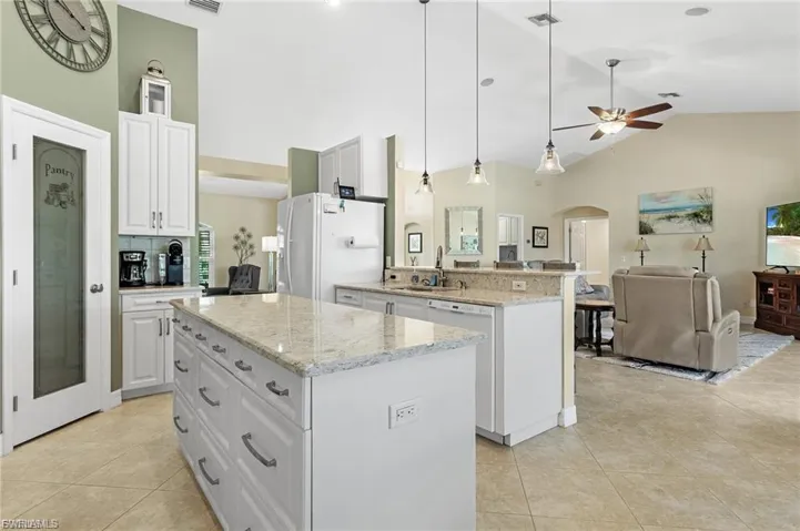 Kitchen featuring white cabinets, arched walkways, open floor plan, decorative light fixtures, and a kitchen island