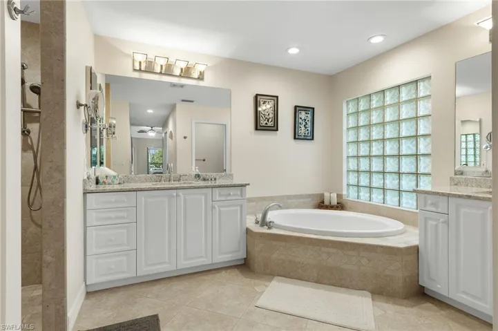 Bathroom with a walk in shower, a bath, two vanities, light tile patterned flooring, and ceiling fan