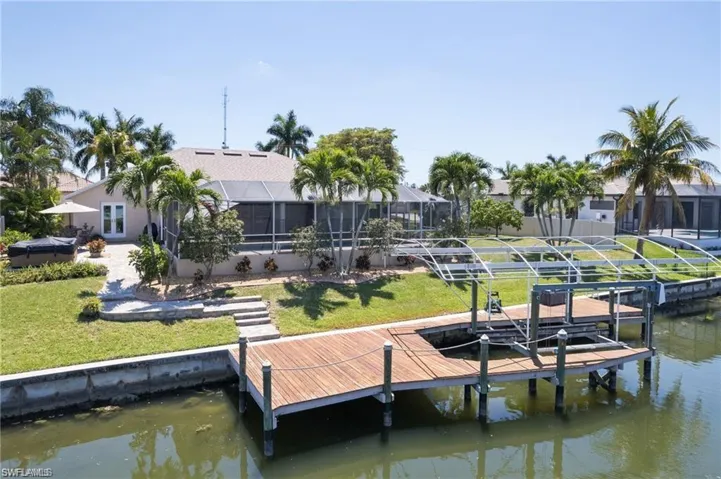 Dock with a water view, boat lift, glass enclosure, and a lawn