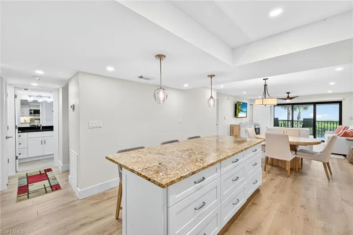 Kitchen with light stone countertops, a breakfast bar area, decorative light fixtures, light wood-style flooring, and recessed lighting
