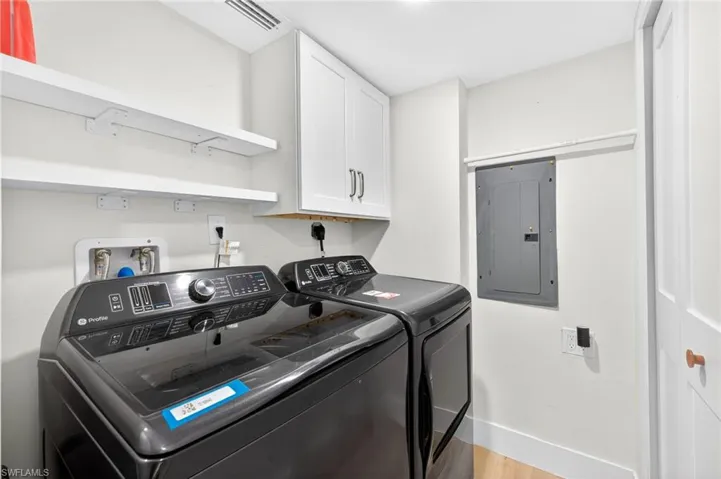 Washroom featuring electric panel, washing machine and dryer, cabinet space, and light wood finished floors